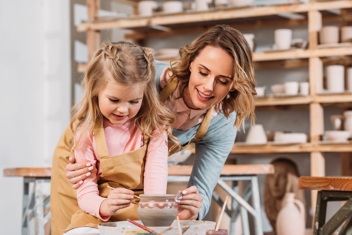 teacher and kid painting ceramic pot in pottery workshop