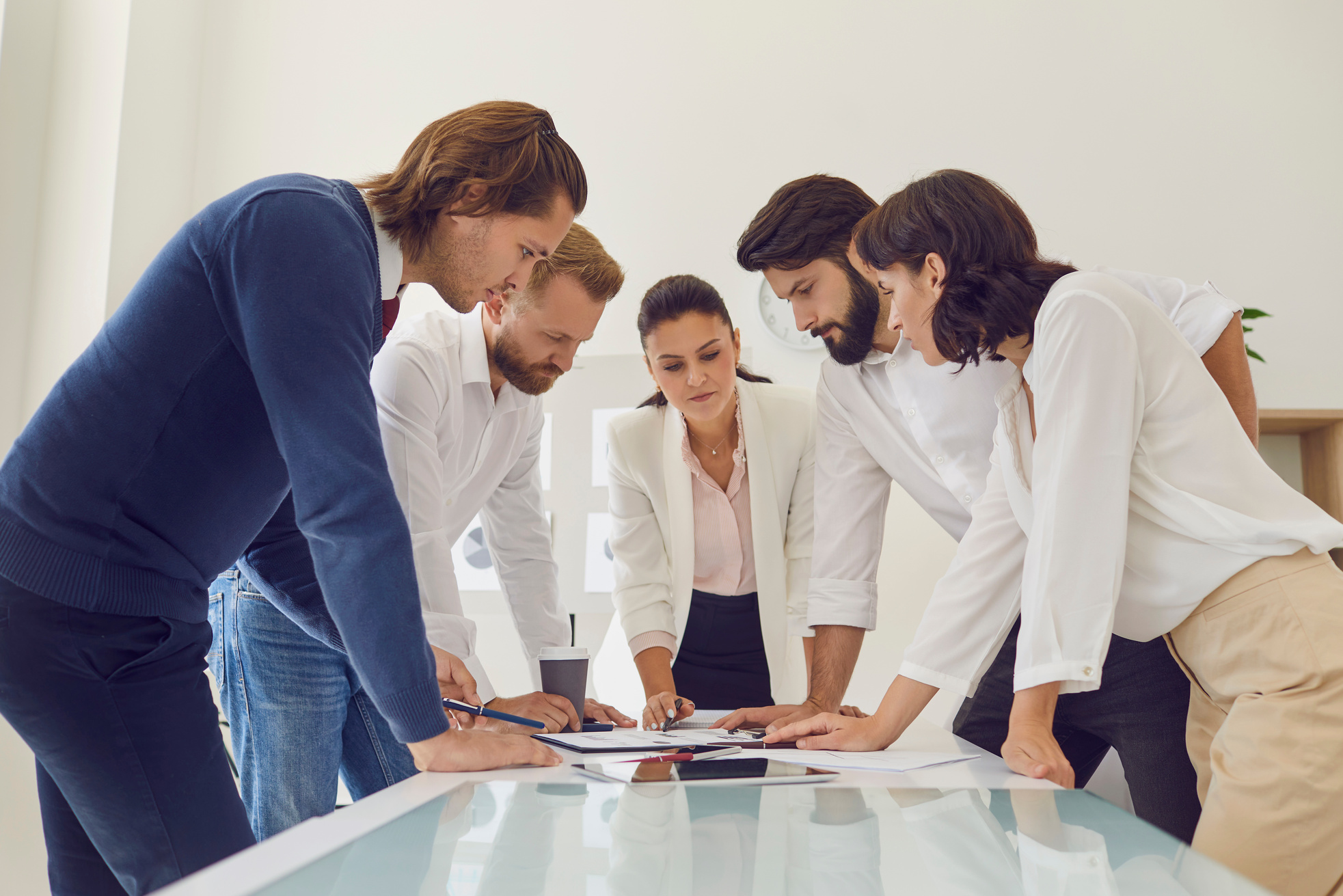 Team of Office Workers Together with Boss Leaning over Table Studying Documents and Reports